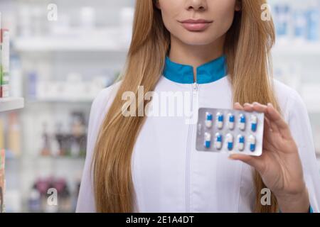 Cropped close up of a female pharmacist holding out pills blister to the camera, copy space. Professional chemist selling medical products at the drug Stock Photo