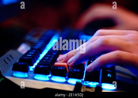Close-up on human hands on a neon lit keyboard. Multifunction keyboard with set of red button. WASD keys are used in many video games.  Stock Photo