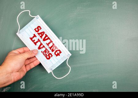 SAVING LIVES. Face mask in a man 's hand. Green chalk board, copy space Stock Photo