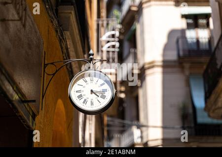 Street clock with arrows on wall with background of buildings in Barcelona Stock Photo
