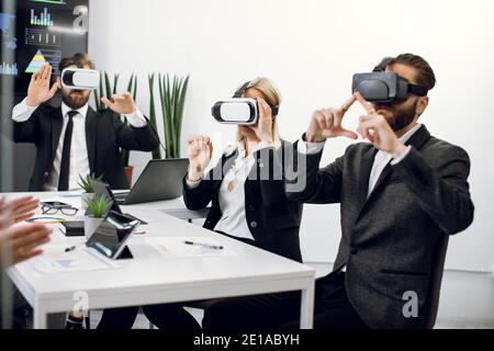 Three diverse business persons sitting at the table in the office with virtual reality headsets, developing a project or testing software. Concept of Stock Photo