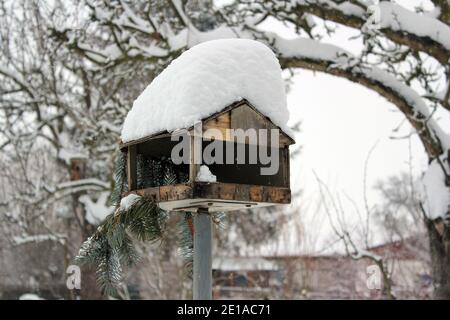 wooden bird house in winter with much snow on its roof Stock Photo