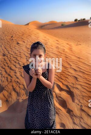 A happy little Indian girl enjoys vacation in dunes in desert and shows heart symbol in hands expressing love in Dubai ,United Arab Emirates