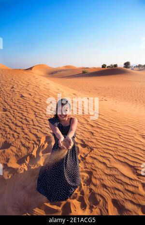 A happy little Indian girl playing in dunes in desert by blowing the sands and enjoying the vacation in Dubai ,United Arab Emirates