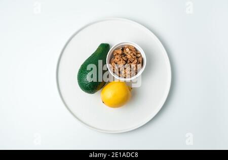Flat white plate with avocado and lemon and walnuts on a white background. Stock Photo