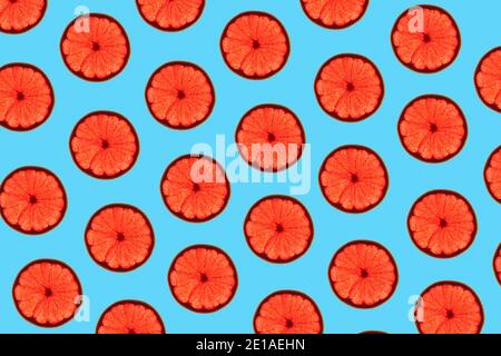 Pattern made of backlit ruby grapefruit slices on blue background Stock Photo