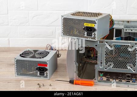 New power supply unit and a screwdriver near tower case with removed old dusty one on a desk. Personal computer PSU replacement. Desktop hardware. Stock Photo
