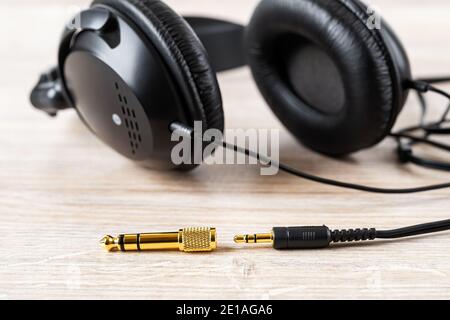 Golden TRS adapter and jack near black wired over ear headphones on a desk. Gold plated plugs for high quality audio. Gadget for listening to music. Stock Photo