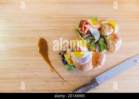 Fully stuffed sandwich, cut in half, with fried quail eggs and green leaves, with a little sauce spilled on side, a cutting knife is placed next to it Stock Photo