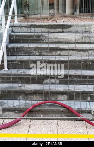 A mesh fence in front of a concrete staircase at a construction site. No entry. Abandoned red electrical plastic cable duct. Occupational safety and h Stock Photo
