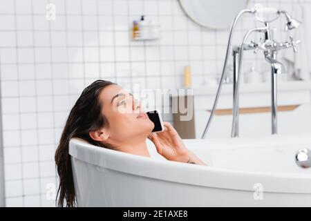 young smiling woman taking bath and talking on cellphone Stock Photo