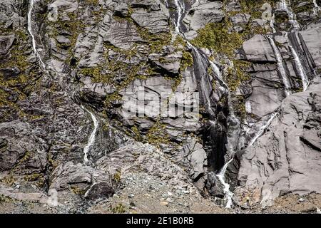 Hikers admiring multiple waterfalls on a cliff face on the road to Milford Sound, South Island, New Zealand Stock Photo
