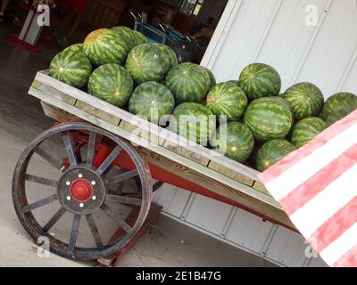 An old wooden cart with metal wheels in front of a country market in the summer is loaded with watermelons for sale. Stock Photo