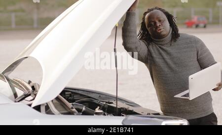 Mobile car assistance. African american black man running diagnostic on broken car on his laptop. High quality photo Stock Photo