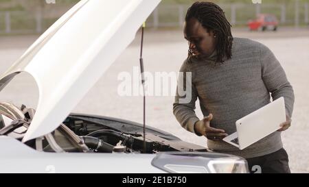 African american black man checking car on roadside and using laptop for diagnostic. High quality photo Stock Photo