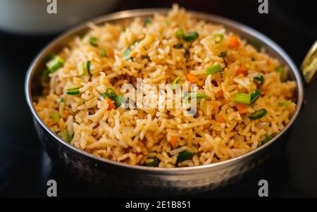 A close up of Vegetable Fried Rice served in a wok pan on a black background.