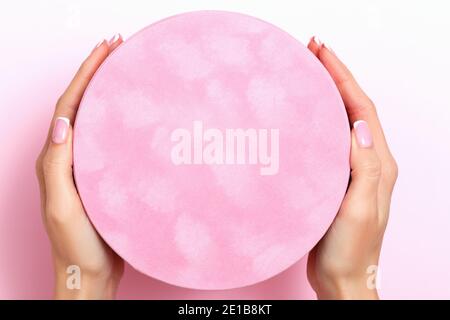 Close-up of female hands holding a large round gift box on a pink pastel background. Birthday valentine's day new year christmas. Stock Photo