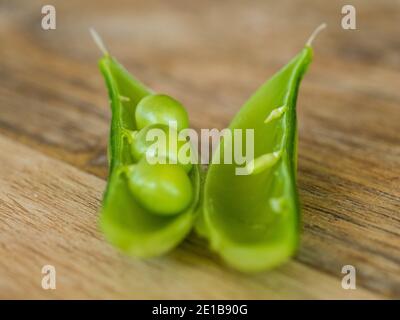 Vegetables, peas in a pod, three green snap peas in an open pod on a wooden kitchen table, fresh and Homegrown, healthy living, Australia Stock Photo