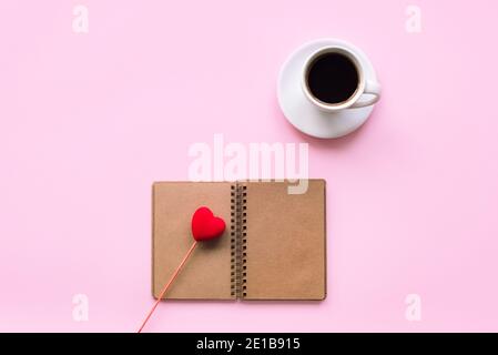 Cup of coffee and a notebook with toy heart on a pink background. Love concept, Valentines day. Top view, flat lay. Stock Photo