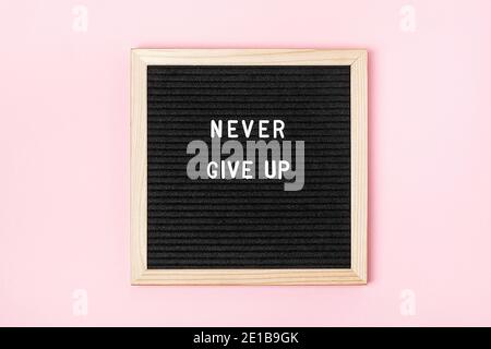 Never give up Motivational quote on black letter board on pink background. Concept inspirational quote of the day. Greeting card, postcard. Stock Photo
