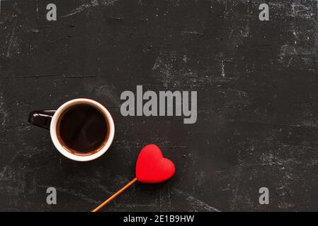 A cup of coffee and toy heart on black background. Valentines day concept. Top view, flat lay, copy space. Stock Photo