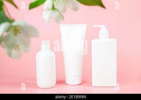 Set of cosmetic for skin care face, body. White blank cosmetics bottles and tube on glass podium and flowering branch, pink background. Natural Organi Stock Photo