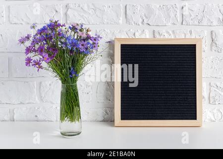 Bouquet blue flowers in vase and blank black letter board on table against white brick wall. Mockup template for your text, design. Concept Women's da Stock Photo