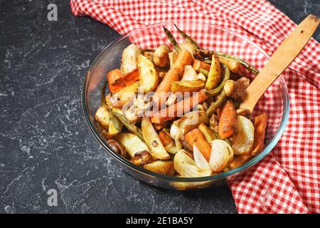 Baked vegetables on black stone background. Potatoes, carrot, mushrooms and onions. Stock Photo