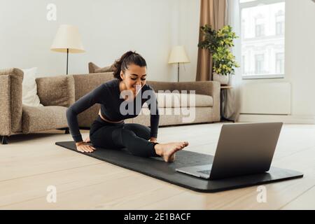 Female doing stretching workout while watching online videos on laptop indoors Stock Photo