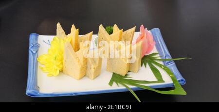 Tamagoyaki or sushi sweet egg with red pickled ginger in a white square ceramic plate on black background, Beautiful decorated Japanese food Stock Photo