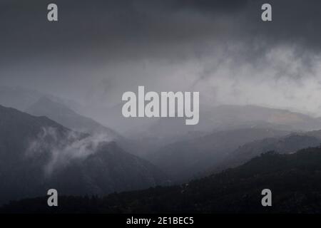 Low clouds lifting up from the mountains in a dark rainy day Stock Photo