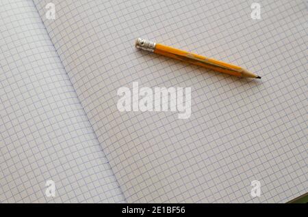 Engineering, accounting, business, education concept. Close-up of an old yellow wooden pencil on blank sheets of an open squared notebook. Selective f Stock Photo