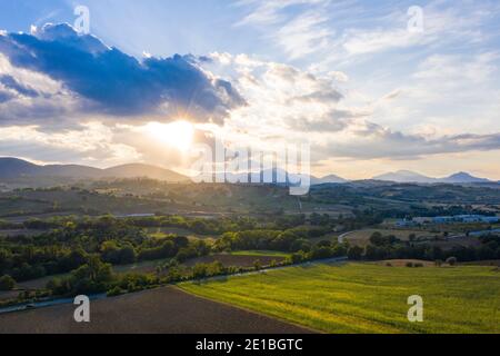 Scenic summer sunset in the hills outside Fabriano, Marche, Italy. The green fields contrast with the blue clouds, the sun is behind the clouds Stock Photo