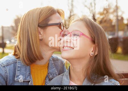 Happy young girl laughing as her mom kissing her on the cheek. Cheerful mother and daughter outdoors in autumn Stock Photo