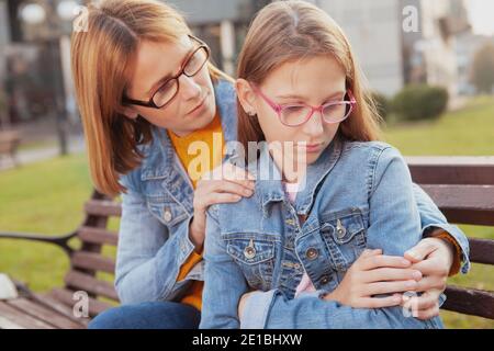 Mature woman comforting her young upset daughter outdoors. Mother and daughter having a fight Stock Photo