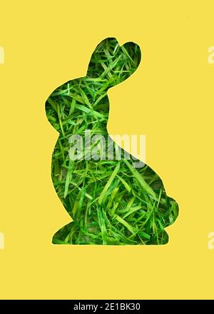 A silhouette of a rabbit is cut out of paper. Background of green grass. Happy Easter greeting card in trendy colors. Yellow and gray are the colors o Stock Photo