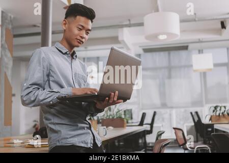 Low angle shot of a concentrated Asian businessman typing on his laptop, working at the office, coy space. Focused male entrepreneur using computer at Stock Photo