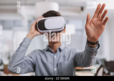 Selective focus on the hand of a man wearing 3d virtual reality headset, reaching out to press button on a hologram. Man using vr goggles with visual Stock Photo