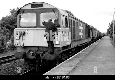 The driver cleaning the windscreen of class 58 diesel locomotive No.58003 heading an empty MGR train at Warwick station, UK. 9th June 1986 Stock Photo