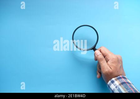 hand holding magnifying glass on blue background  Stock Photo