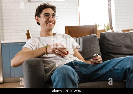 Picture of happy optimistic handsome man indoors at home watching tv Stock Photo