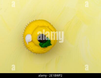 Overhead view of a freshly frosted cupcake on a yellow background. Stock Photo