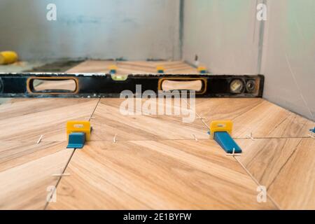 Tiling work. The man checks the level of the correct laying of the floor tiles. Stock Photo