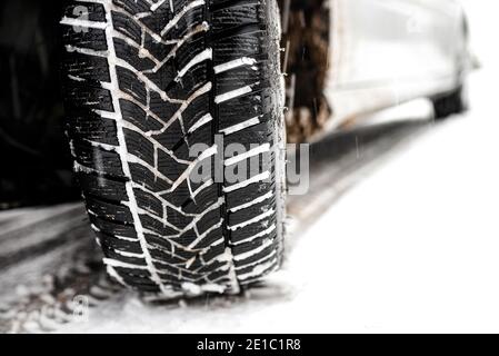 New winter tire in a silver car standing on a snow-covered road in the forest, a visible tread with snow.