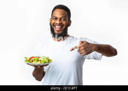 Cheerful Black Guy Pointing Finger At Salad Over White Background Stock Photo