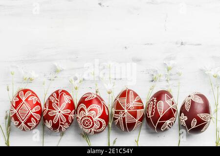 Row of red and white handmade wax dyed Easter eggs. Ukrainian pysanka frame on white wooden background with copy space for text Stock Photo