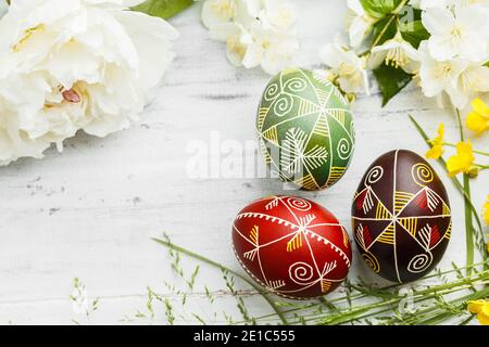 Three handmade Easter eggs decorated with wax-resist dyeing technique. Ukrainian pysanka on white shabby wooden background with empty space for text Stock Photo