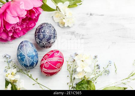 Three handmade painted Easter eggs with spring flowers. Ukrainian pysanka decorated with wax-resist dyeing technique on white shabby wooden background Stock Photo