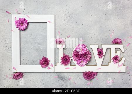 Floral Greeting card. Creative layout made of empty photo frame, colorful flowers and word LOVE on gray stone background. Love concept. Flat lay.