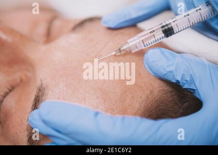 Close up cropped shot of a professional cosmetologist using syringe with face filler, doing cosmetic injections in the skin of mature male client Stock Photo